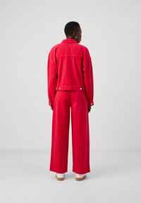 Rød denimjakke og vide bukser med en afslappet pasform, trykknapper og subtile syninger, parret med hvide fodtøj.