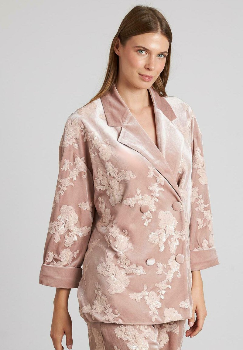 Chaqueta de terciopelo rosa con bordados florales, diseño cruzado, amplios solapas y mangas de tres cuartos. Textura suave y detalles elegantes.