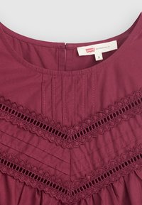 Abito bordeaux con scollatura rotonda, caratterizzato da pieghe verticali e rifiniture in pizzo a motivo chevron. L'etichetta mostra il marchio "Levi's," taglia S.