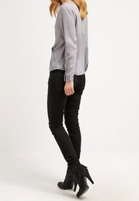 Blusa grigia a maniche lunghe con una vestibilità leggermente ampia e tasche laterali, abbinata a jeans skinny neri e stivaletti neri con tacco alto.