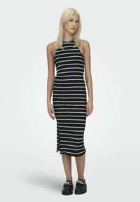 Vestido midi a rayas en blanco y negro con cuello alto, diseño sin mangas, abertura lateral y textura acanalada. Combinado con zapatos negros de suela gruesa.