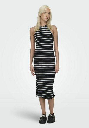 Vestido midi a rayas en blanco y negro con cuello alto, diseño sin mangas, abertura lateral y textura acanalada. Combinado con zapatos negros de suela gruesa.