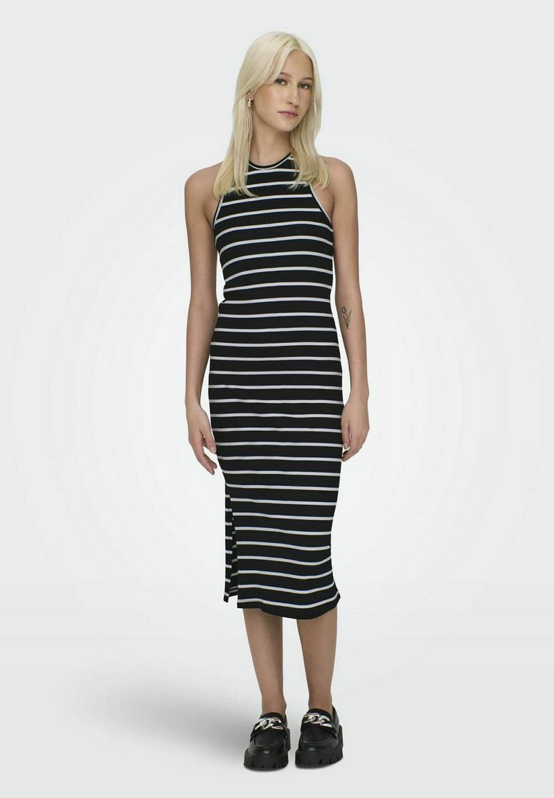 Vestido midi a rayas en blanco y negro con cuello alto, diseño sin mangas, abertura lateral y textura acanalada. Combinado con zapatos negros de suela gruesa.