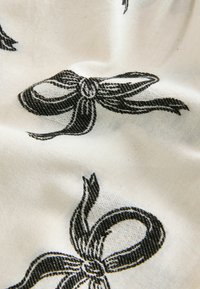 White fabric featuring a repeating pattern of black bows with textured detailing. The bows have defined loops and twists, creating a subtle design.