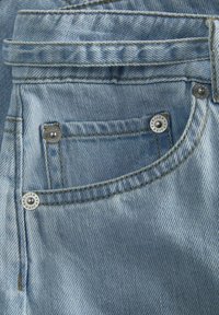 Kapsa z lehce modrého denimu s viditelným prošitím a kovovými nýty na rozích kapsy a v oblasti poutka na opasek.