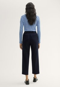 Gestreepte langekoestop in lichtblauw met marineblauwe strepen, gecombineerd met marineblauwe wijde broek met een elastische tailleband en zakken.