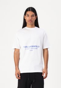 Λευκό βαμβακερό T-shirt με εκτυπωμένο μπλε λογότυπο που γράφει "KARL LAGERFELD 21 RUE ST-GUILLAUME PARIS," με χαλαρή εφαρμογή και στρογγυλή λαιμόκοψη.
