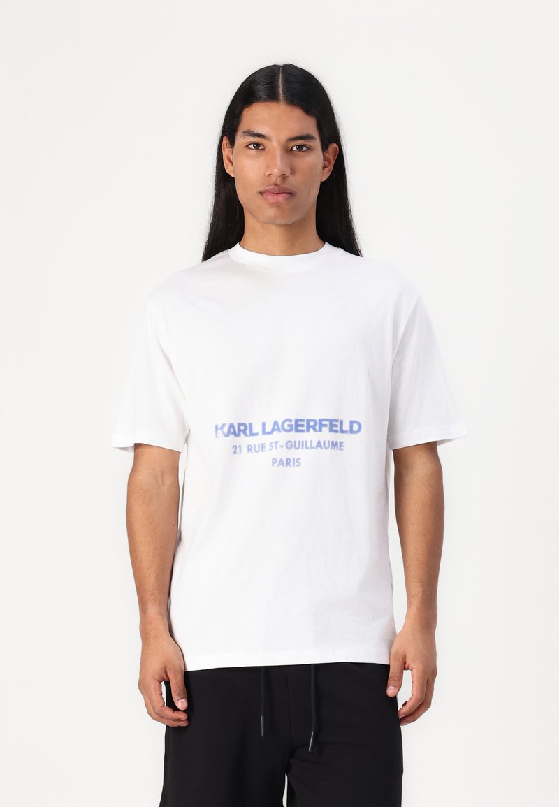 Λευκό βαμβακερό T-shirt με εκτυπωμένο μπλε λογότυπο που γράφει "KARL LAGERFELD 21 RUE ST-GUILLAUME PARIS," με χαλαρή εφαρμογή και στρογγυλή λαιμόκοψη.