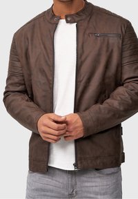 Veste en cuir marron avec fermeture éclair à l'avant, col à pression et accent de épaules matelassé. Comprend deux poches latérales et une poche zippée sur la poitrine.