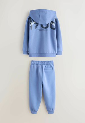 Világoskék pulóver és hozzá illő, puha anyagból készült melegítőnadrágok, kapucnival, bordázott mandzsettákkal és hátoldalán hangsúlyos szöveges mintával.