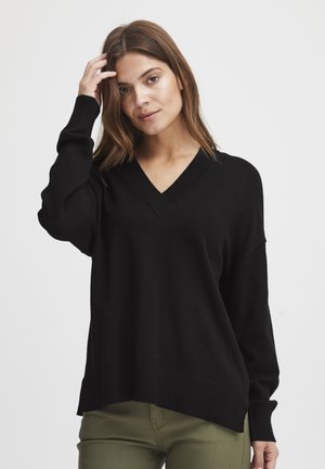 Pull noir à col en V avec des manches longues et des poignets côtelés. Texture douce avec une coupe décontractée, présentant un ourlet à l'arrière légèrement plus long.