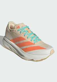 Scarpa da corsa beige con lacci turchesi, strisce arancioni, suola bianca imbottita e branding arancione sulla linguetta e sul lato, inclinata per mostrare il lato esterno.