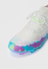 Chuteira de futebol branca com um cabedal texturizado, apresentando um design degradé em azul, roxo e verde na ponta, fixada com atacadores brancos.