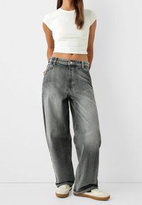 Dżinsy o szerokich nogawkach i wysokim stanie, wykonane z wyblakłego szarego denimu o lekko postarzanej fakturze. Połączone z białym krótkim topem i jasnymi trampkami.