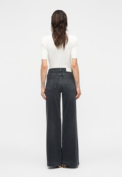 Τζιν ψηλόμεσο, με φαρδιά μπατζάκια σε σκούρο γκρι τζιν ύφασμα. Διαθέτει δύο πίσω τσέπες και ετικέτα στη μέση, συνδυασμένο με εφαρμοστή λευκή μπλούζα.