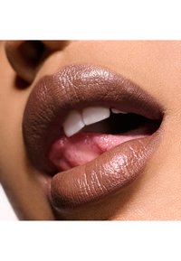 Zbliżenie na usta z matową brązową pomadką i błyszczącym różowym wnętrzem warg, ukazującym białe zęby. Tekstura skóry jest gładka i jednolita.