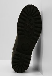 Semelle de bottes en caoutchouc noir avec des rainures profondes et une forme arrondie. Présente un logo circulaire et un marquage de taille 37. Texturée pour une meilleure adhérence.