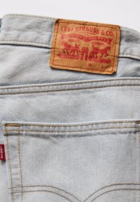 Ljusblå jeans i denim med brun läderlapp med rödtryckt logotyp. Kontraststickning och två bakfickor synliga.