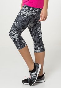Leggings Capri en estampado de camuflaje digital en negro y gris, confeccionados con tela elástica, combinados con zapatillas de correr negras con acentos blancos.