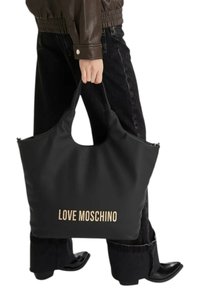Borsa tote nera con una texture morbida, dotata di manico ritagliato e logo "LOVE MOSCHINO" in oro a contrasto. Indossata da una persona con jeans scuri.