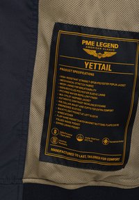 Chaqueta de popelín de poliéster en color navy con etiquetas amarillas. Las características incluyen forro de malla, cuello acanalado, mangas confeccionadas y múltiples bolsillos.