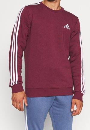 Mørkerød sweatshirt med hvide striber ned ad ærmerne, rund hals, ribstrikkede ærmegab og kant. Adidas-logo på brystet, lavet af behageligt stof.