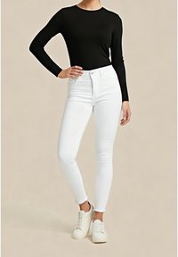 Top negro de manga larga combinado con jeans pitillo blancos de talle alto. Zapatillas blancas con punteras redondeadas completan el conjunto, sobre un fondo neutro.