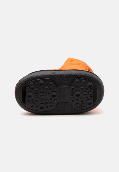Semelle en caoutchouc noir avec motifs circulaires en relief pour l'adhérence sur une botte d'hiver orange vue de dessous.
