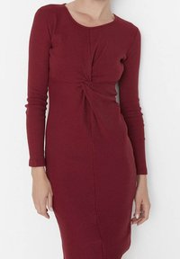 Robe bordeaux à manches longues avec un détail frontal enroulé, fabriquée en tissu côtelé, présentant une silhouette ajustée et une longueur au genou.