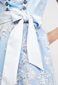 Robe bleu clair avec motifs floraux brodés et un nœud en satin blanc à la taille. Comprend des éléments en métal argenté et des détails en dentelle délicate.