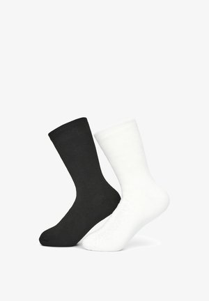 Calzini in cotone bianchi e neri, di lunghezza media, con texture a coste, ciascuno con un design semplice e colori a contrasto, esposti affiancati.