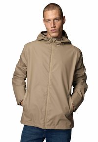 Beige wasserdichte Jacke mit Reißverschluss auf der Vorderseite, verstellbarem Kapuze und Seitentaschen, mit glatter Textur und lockerer Passform.