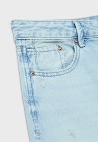 Lyseblå cowboybukser med frynset kant, der har en forlomme, synlige sømme og små slidte detaljer.