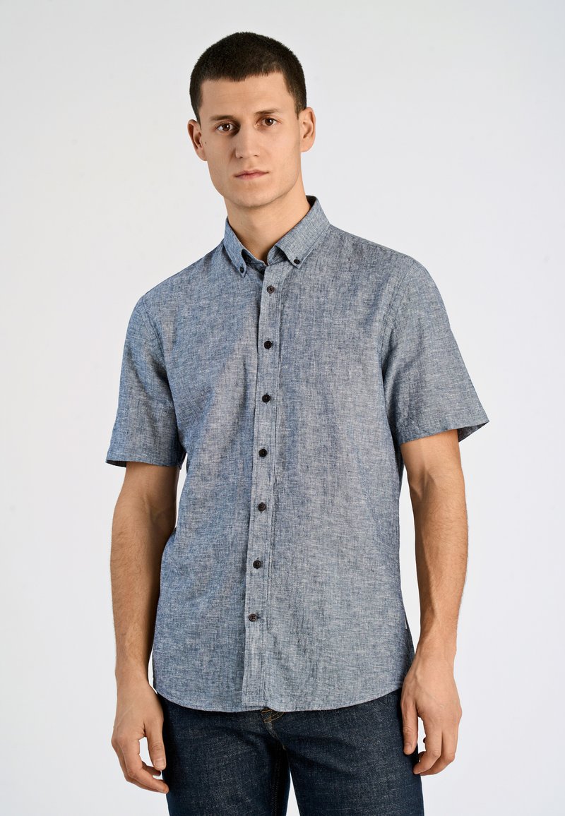 Camicia a maniche corte con bottoni, realizzata in tessuto chambray blu con una texture sottile; presenta bottoni marroni e un colletto a punta.