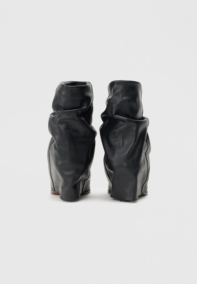 Schwarze Leder-Ankle Boots mit einer knitterigen Textur, die ein weiches, lässiges Design und eine abgerundete Zehenpartie aufweisen. Flache Sohlen mit minimaler Verzierung.