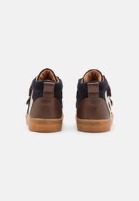 Para bucików dla malucha wykonanych z granatowego materiału, z brązowymi skórzanymi obcasami, beżowymi gumowymi podeszwami i bocznymi paskami, widoczna z tyłu na białym tle.