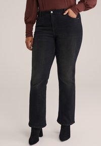 Črne denim hlače ravnega kroja s srednjim pasom, ki imajo sprednji žep in subtilno zbledelo teksturo, v kombinaciji z črnimi gležnjarji.