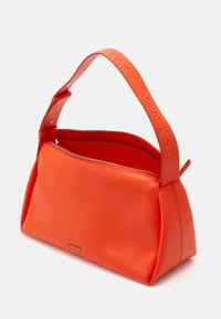Calvin Klein narancssárga kézi táska sima bőrből, szilárd formával és széles vállpánttal, amelyen a márka dombornyomott felirata található. Cipzáros fő rekesz.