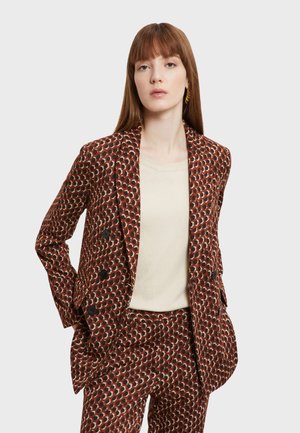 Blazer croisé marron avec un motif géométrique en crème et noir, associé à une chemise crème. Tissu lisse, coupe ajustée.