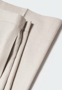 Tissu en lin beige plié avec des coutures visibles et une texture douce sur un fond clair uni.