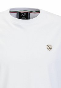 Witte katoenen t-shirt met ronde hals; heeft een klein geborduurd schildlogo met "1969" en "ITALIA" op de linkerkant van de borst.