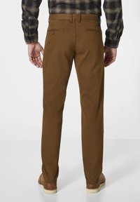 Brown cotton trousers with a straight fit, two back pockets, and a flat front. Worn with a plaid shirt and brown footwear.