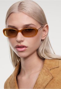 Braune rechteckige Sonnenbrille mit getönten Gläsern, Kunststoffrahmen und glatter Textur. Getragen mit einem beigen, strukturierten Blazer.