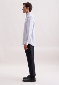 Camicia azzurro chiaro a scacchi, vestibilità rilassata, maniche lunghe con polsini, abbinata a pantaloni scuri su misura e scarpe nere con lacci.