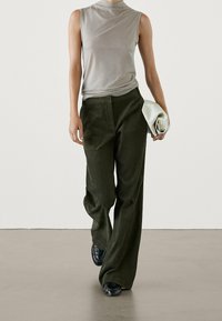 Haut gris sans manches, pantalon vert à jambes larges, et chaussures noires. Le modèle tient une pochette blanche. Tissu lisse avec une texture subtile.