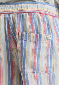 Gestreifte Stoffshorts in Blau, Rot und Gelb. Verfügt über einen elastischen Bund und eine aufgesetzte Tasche auf der rechten Seite. Markenetikett sichtbar.