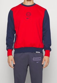 Sweat-shirt à col rond rouge et marine avec un graphique de basketball et le logo Nike. Dispose de poignets et d'un ourlet côtelés, en matière douce composée de coton mélangé.