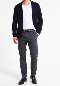 Navy blazer with two buttons, white T-shirt, gray chinos, and black leather dress boots. Smooth fabric with tailored fit.