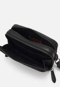 Cartera de cuero negro con cremallera y múltiples compartimentos. Presenta una textura suave, costuras en contraste y un adorno de llavero desmontable.
