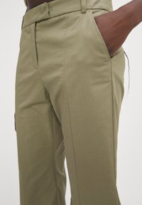 Pantalons vert olive avec une coupe cintrée, poches latérales et une texture lisse. Dotés d'une braguette zippée et de passants de ceinture pour un ajustement réglable.